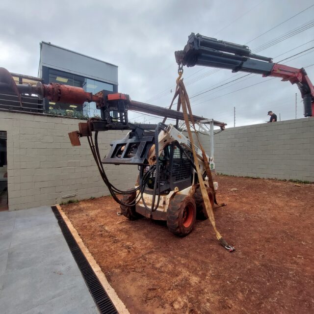 Mini carregadeira com perfuratriz sendo içada